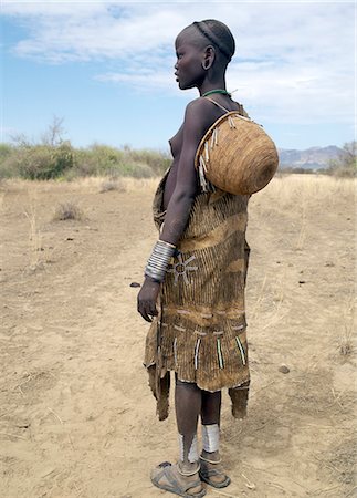 A Mursi girl dressed in finely decorated leather garments with a beautifully made basket over one shoulder. Her partially shaven head is the typical hairstyle of her tribe.The Mursi speak a Nilotic language and have affinities with the Shilluk and Anuak of eastern Sudan. They live in a remote area of southwest Ethiopia along the Omo River, the country's largest river. Foto de stock - Con derechos protegidos, Código: 862-03820560