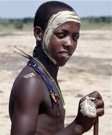 Un garçon de Samburu la veille de sa circoncision.Il a sélectionné le côté droit de son visage et le corps avec de l'argile blanche tout en attirant l'eau d'une source qui ne tarit jamais. Chaque garçon procédera à cet effet un nouveau conteneur de Gourde en forme fait par sa mère du bois évidée. Photographie de stock - Rights-Managed, Code: 862-03820694