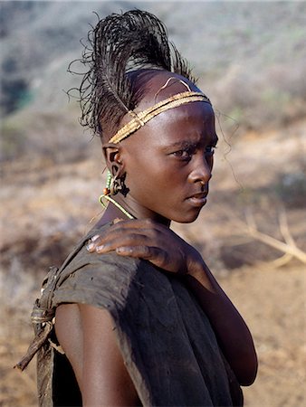 simsearch:862-03820358,k - Kenya, South Horr, Kurungu.A Samburu youth after his circumcision. The day after he has been circumcised, the initiate must hang in his pierced earlobes copper ear ornaments that are normally worn by married women. His sponsors make him a new headdress of ostrich feathers fastened to a narrow band of plaited fibre, which fits tightly round his forehead like a sweatband. Stock Photo - Rights-Managed, Code: 862-03820696