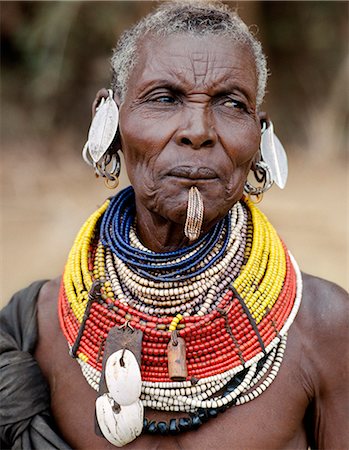 An old Turkana woman wearing all the finery of her tribe.In a hole pierced below her lower lip, she wears an ornament beautifully made from twisted strands of copper wire.Leaf shaped ear ornaments are typically worn by married women of the tribe and the tiny amber coloured rings hanging from her earrings are made from goats hooves. Foto de stock - Con derechos protegidos, Código: 862-03820731