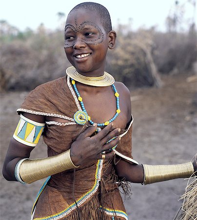república unida de tanzania - A Datoga woman relaxes outside her thatched house.The traditional attire of Datoga women includes beautifully tanned and decorated leather dresses and coiled brass armulets and necklaces. Extensive scarification of the face with raised circular patterns is not uncommon among women and girls. Foto de stock - Con derechos protegidos, Código: 862-03821003