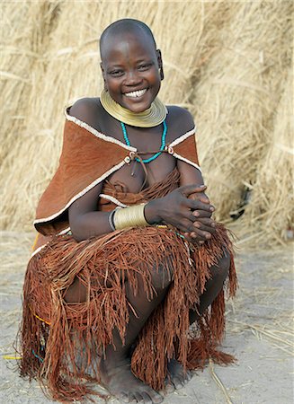 A Datoga woman relaxes outside her thatched house.The traditional attire of Datoga women includes beautifully tanned and decorated leather dresses and coiled brass armbands and necklaces.Scarification of the face is not uncommon among women and girls. Stock Photo - Rights-Managed, Code: 862-03821031