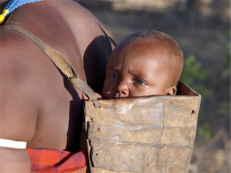 A Datoga baby is carried in a leather carrier on his mothers back  The traditional attire of Datoga women includes beautifully tanned and decorated leather dresses and coiled brass ornaments of every description. Stock Photo - Rights-Managed, Code: 862-03821033
