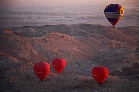 3 No. red and 1 No. multicoloured hot air balloons, ascend at dawn over the Valley of the Kings and Queens, Al Asasif, Luxor, Egypt, Africa. Fotografie stock - Rights-Managed, Codice: 862-03887585