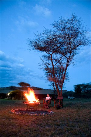 simsearch:862-03808668,k - Tanzania, Serengeti. A tourist warmsup by the fire after a safari at Lemala Ewanjan. Foto de stock - Con derechos protegidos, Código: 862-03890058