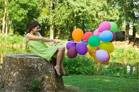 simsearch:877-06836460,k - Young woman holding bunch of balloons, sitting on tree stump Photographie de stock - Rights-Managed, Code: 877-06834309