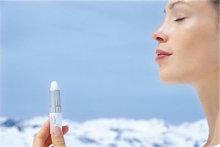 Portrait of young woman holding chap stick, eyes closed, snowy mountains at the back, side view, blue sky Foto de stock - Con derechos protegidos, Código: 877-06835903