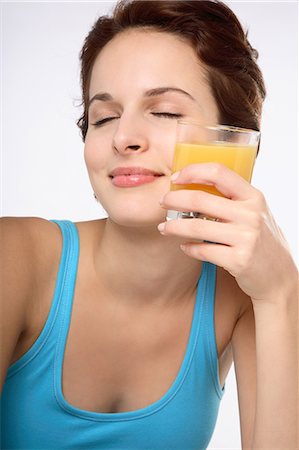 simsearch:877-06834718,k - Portrait of a young brunette woman eyes closed smiling holding a glass of fruit juice against left cheek Stock Photo - Rights-Managed, Code: 877-06836389