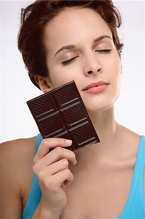 Portrait of a young brunette woman eyes closed holding bar of chocolate against face Photographie de stock - Rights-Managed, Code: 877-06836390