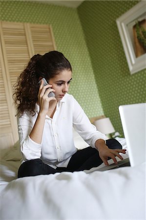 A teenage girl phoning and consulting her laptop on her bed Stock Photo - Rights-Managed, Code: 877-08128011
