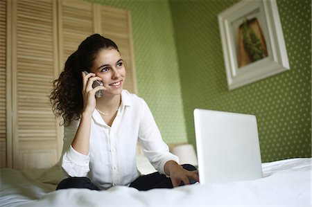 A teenage girl phoning and consulting her laptop on her bed Stock Photo - Rights-Managed, Code: 877-08128012