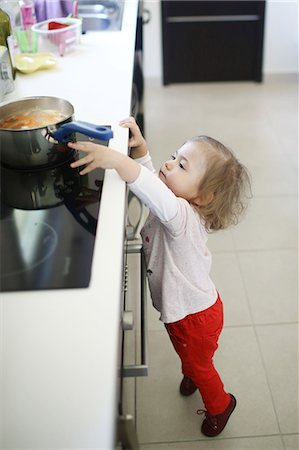 dangerous accident - A 2 years old little girl is about to catch a saucepan on the hob Foto de stock - Con derechos protegidos, Código: 877-08129098