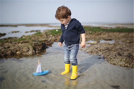 A 3 years old boy plays with a wooden boat on the beach Foto de stock - Con derechos protegidos, Código: 877-08129118