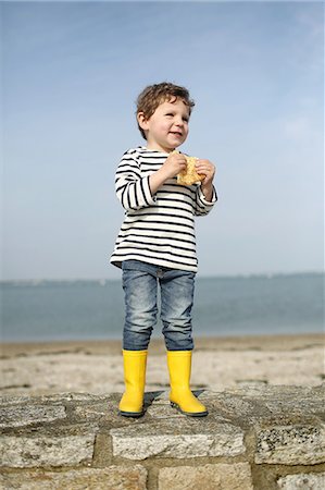 3 years old boy eating a crepe at the beach Foto de stock - Con derechos protegidos, Código: 877-08129124