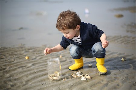 3 years old boy looking for sea shells on the beach Foto de stock - Con derechos protegidos, Código: 877-08129120