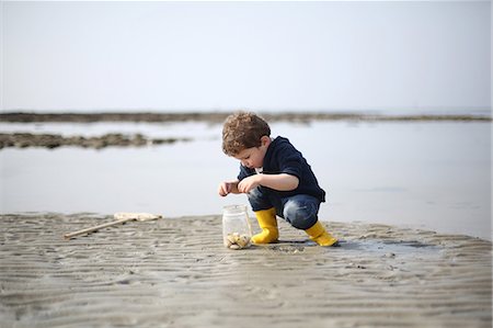 3 years old boy looking for sea shells on the beach Foto de stock - Con derechos protegidos, Código: 877-08129121