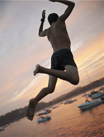 A boy leaping off the dock into the water, at sunset on the coast. Foto de stock - Con derechos protegidos, Código: 878-07442510