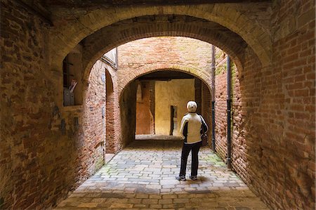 A tourist observes the architecture of a street in the historic center of Buonconvento. Buonconvento, Ombrone valley,Crete senesi, Siena province, Tuscany, Italy, Europe Foto de stock - Con derechos protegidos, Código: 879-09033131