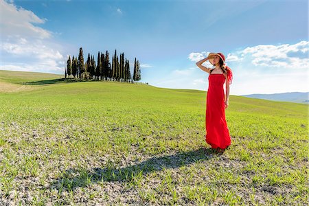 simsearch:879-09100804,k - San Quirico d'Orcia, Orcia valley, Siena, Tuscany, Italy. A young woman in red dress admiring the view in a wheat field near the cypresses of Orcia valley Stock Photo - Rights-Managed, Code: 879-09099963