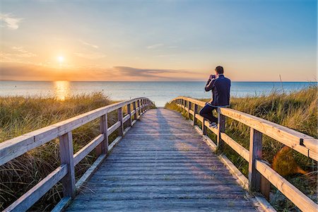 schleswig-holstein - Weissenhäuser Strand, Ostholstein, Schleswig-Holstein, Germany. Man photographing the sunset on a pier to the Baltic Sea. Fotografie stock - Rights-Managed, Codice: 879-09100430