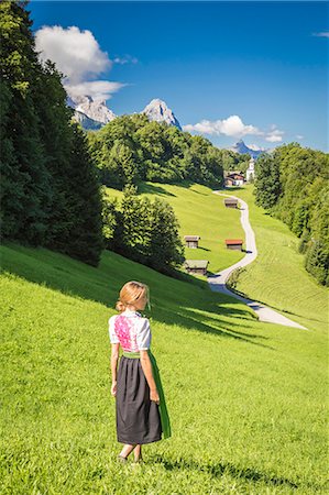 simsearch:879-09100966,k - A girl in Typical Bayern dress walking in front of Wamberg village, with Mount Zugspitze and Waxenstein on the background. Garmisch Partenkirchen, Bayern, Germany. Fotografie stock - Rights-Managed, Codice: 879-09100952