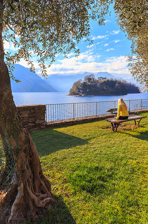 A girl ditting on a bench in front of the Comacina Island, Ossuccio, Como Lake, Lombardy, Italy, Europe. Stock Photo - Rights-Managed, Code: 879-09189612