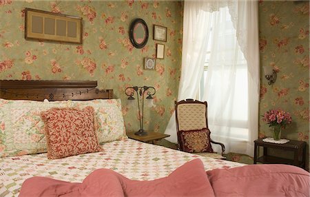 Bedroom with double bed, wooden chair, floral decor and old pictures on wall. Stock Photo - Rights-Managed, Code: 872-08914849