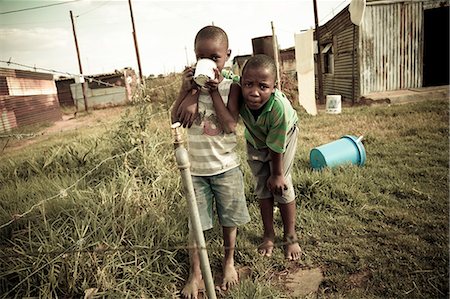 simsearch:873-06675608,k - Two young black boys stand together in a rural township, drinking water and looking at camera Fotografie stock - Rights-Managed, Codice: 873-06675190